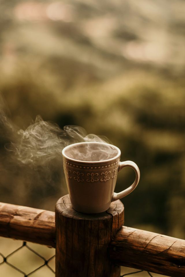 taza de café caliente sobre un barandal de madera